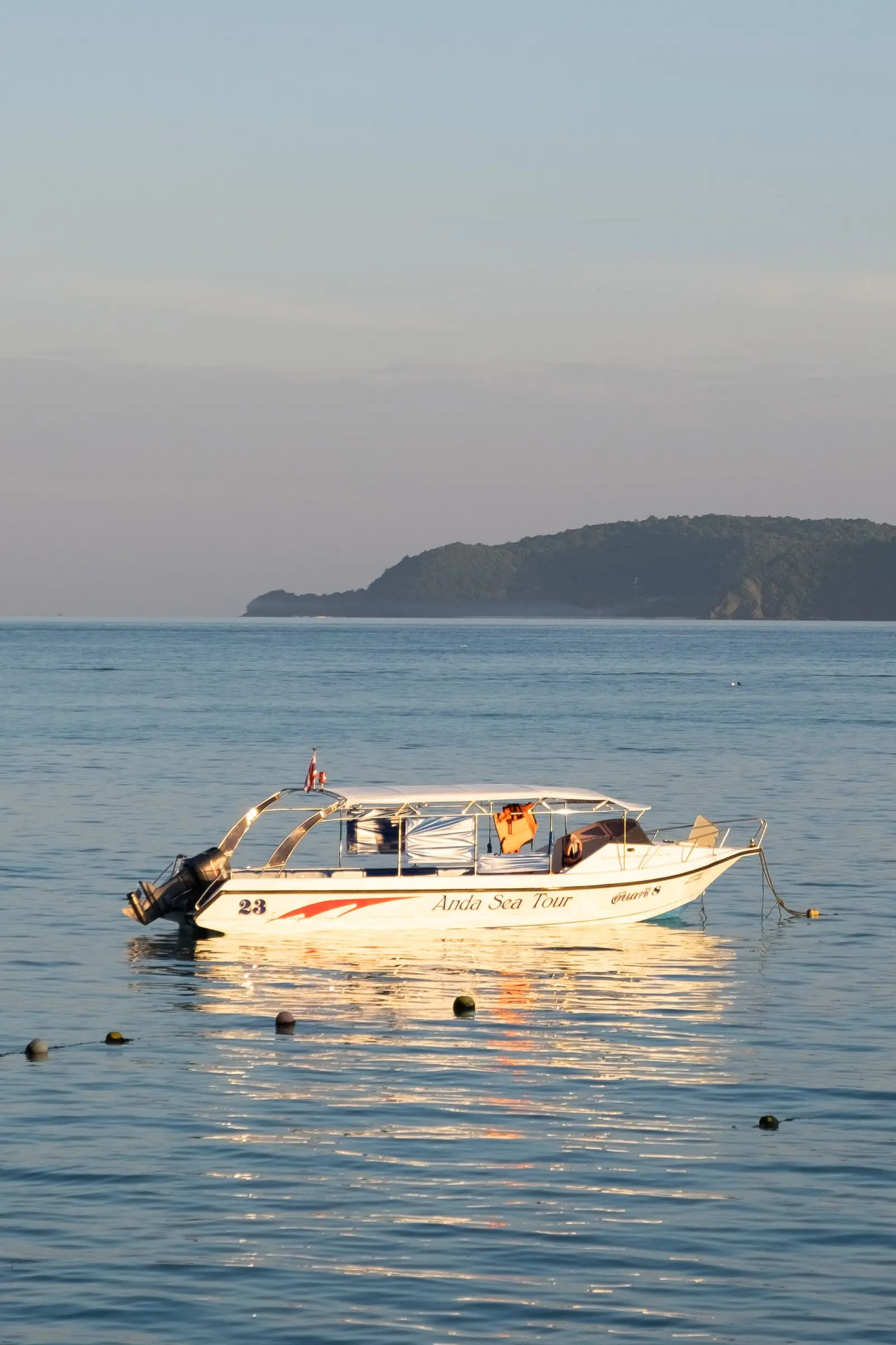 A white motorboat on calm water with hills behind at sunrise