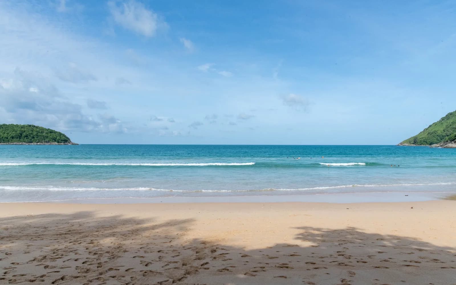 Nai Harn Beach under clear blue skies with gentle waves.