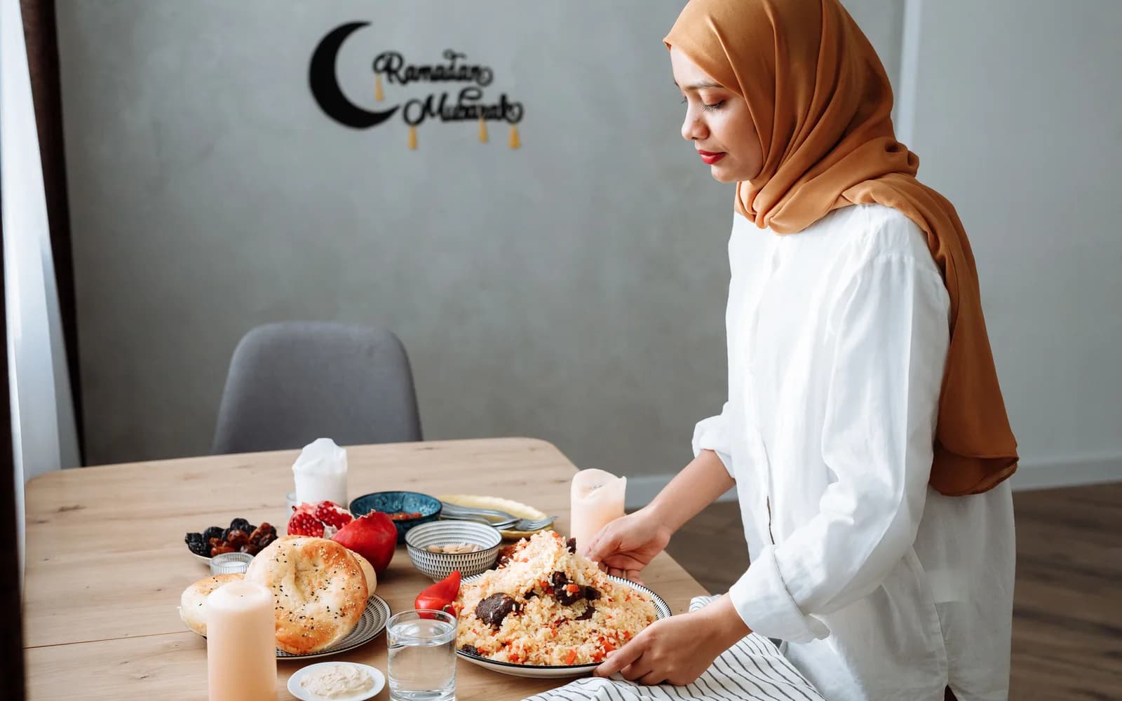 A woman in a hijab setting a table with traditional iftar food during Ramadan