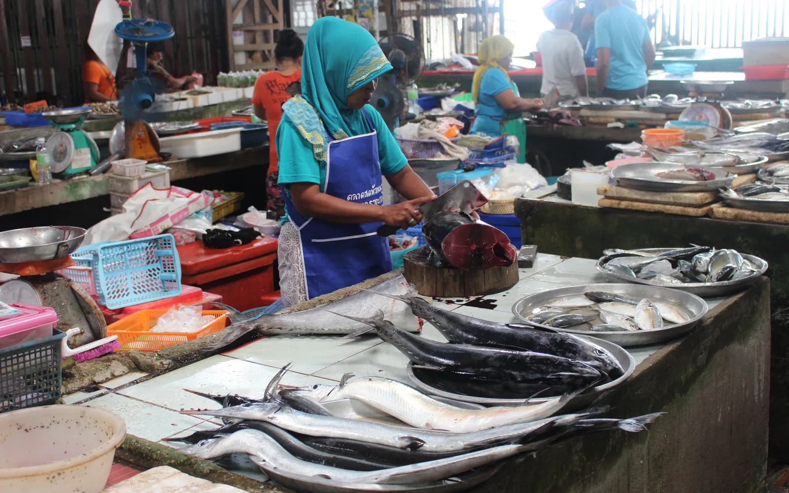 A woman in a headscarf preparing fresh fish at a Thai wet market.